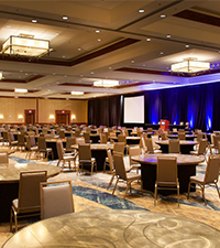 Elegant ballroom venue arranged with tables, chairs, decorative lighting, and a stage