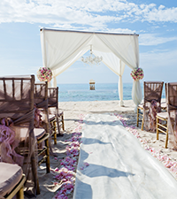Decorated beach wedding ceremony setup overlooking the sea under a bright blue sky