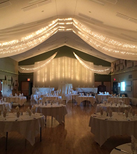 Community hall decorated with lights, drapes, tables, and seating for a special event
