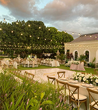 Outdoor garden venue arranged with dining tables, chairs, flowers, and string lights